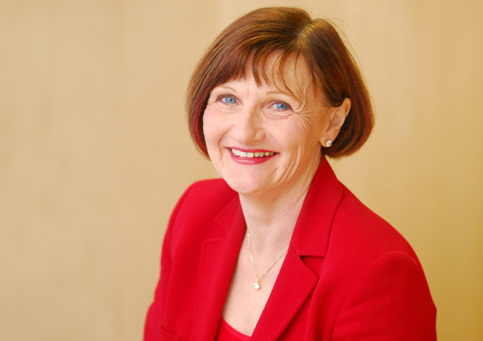 A photograph of Dame Barbara Hakin wearing a red jacket and a red top.