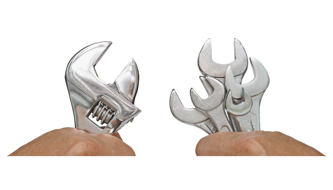 Image showing two hands holding different tool options against a plain white background. On the left, a single adjustable spanner is held upright. On the right, a hand grips a small collection of various spanners grouped together. The visual suggests a comparison between a single versatile tool and multiple specialised tools, symbolising choice, flexibility and different approaches to solving problems.