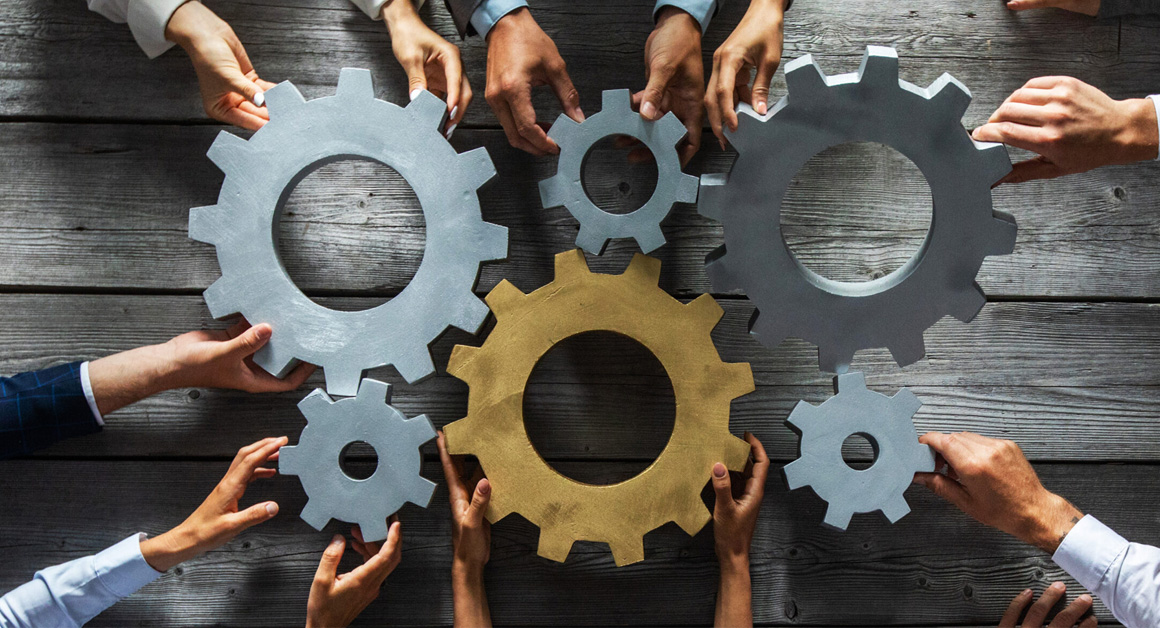 Group of business people joining together silver and golden coloured gears on table at workplace top view