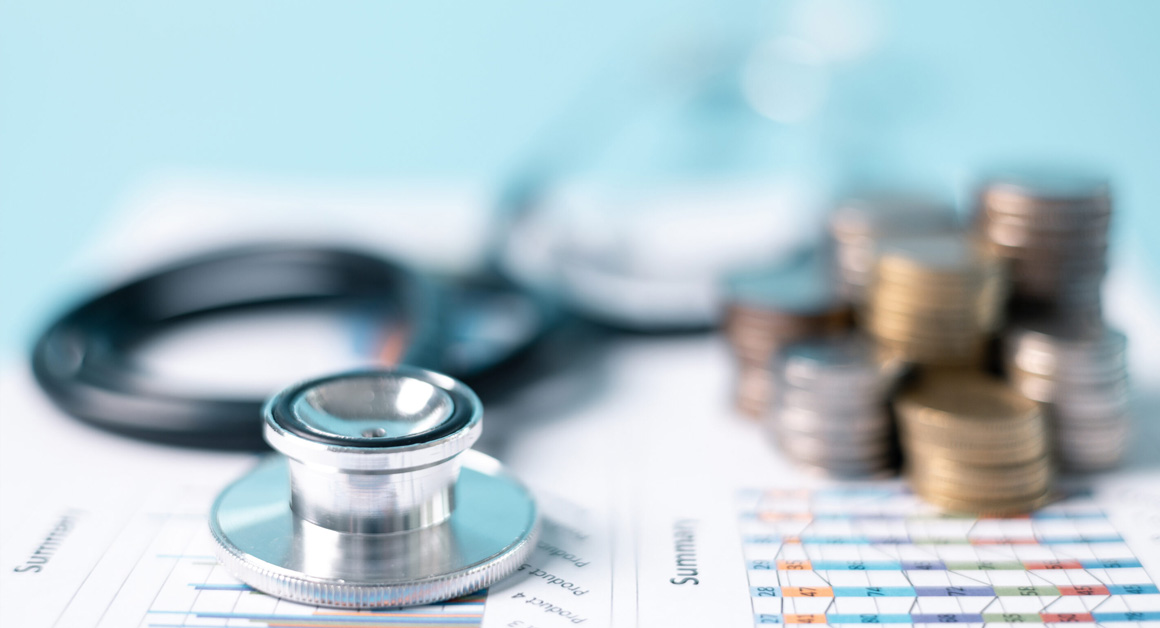 A stock image of a report with some blurred stacks of coins and a stethoscope on top of it.