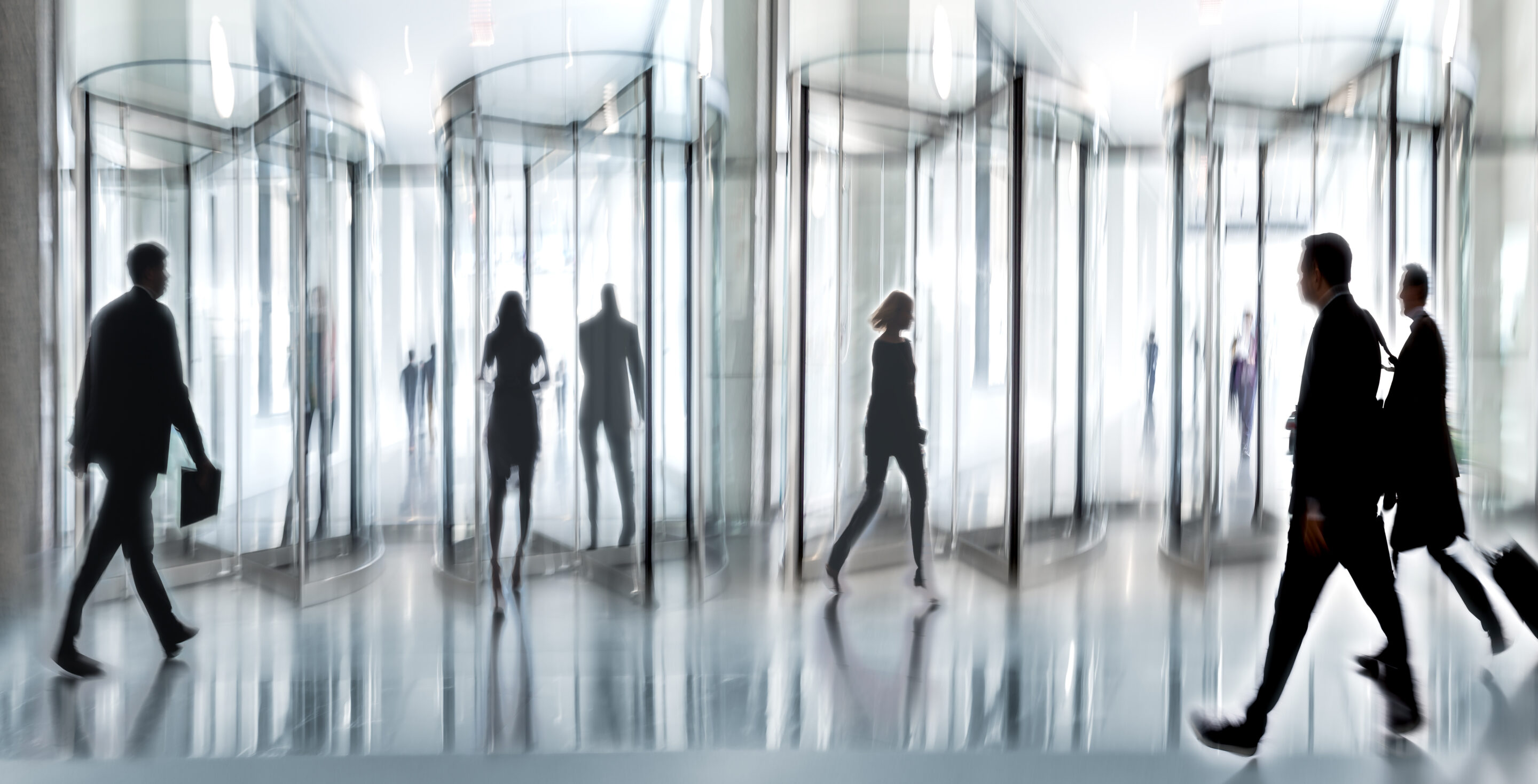 Blurred image showing people entering and exiting a revolving office glass door.