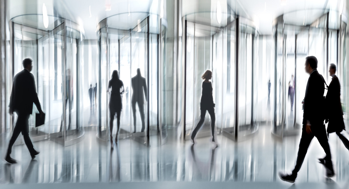Image shows people entering and exiting a revolving office glass door.