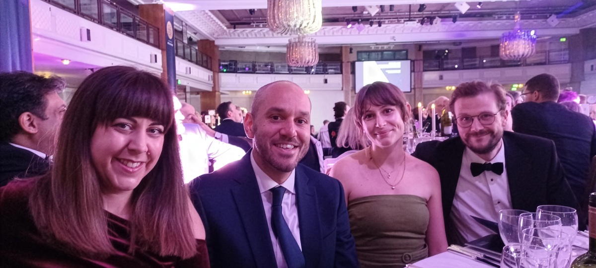 Four IMPOWER finalists seated together at the 2025 MCA Awards Ceremony, dressed in formal evening attire at a banquet-style event with chandeliers and purple ambient lighting.